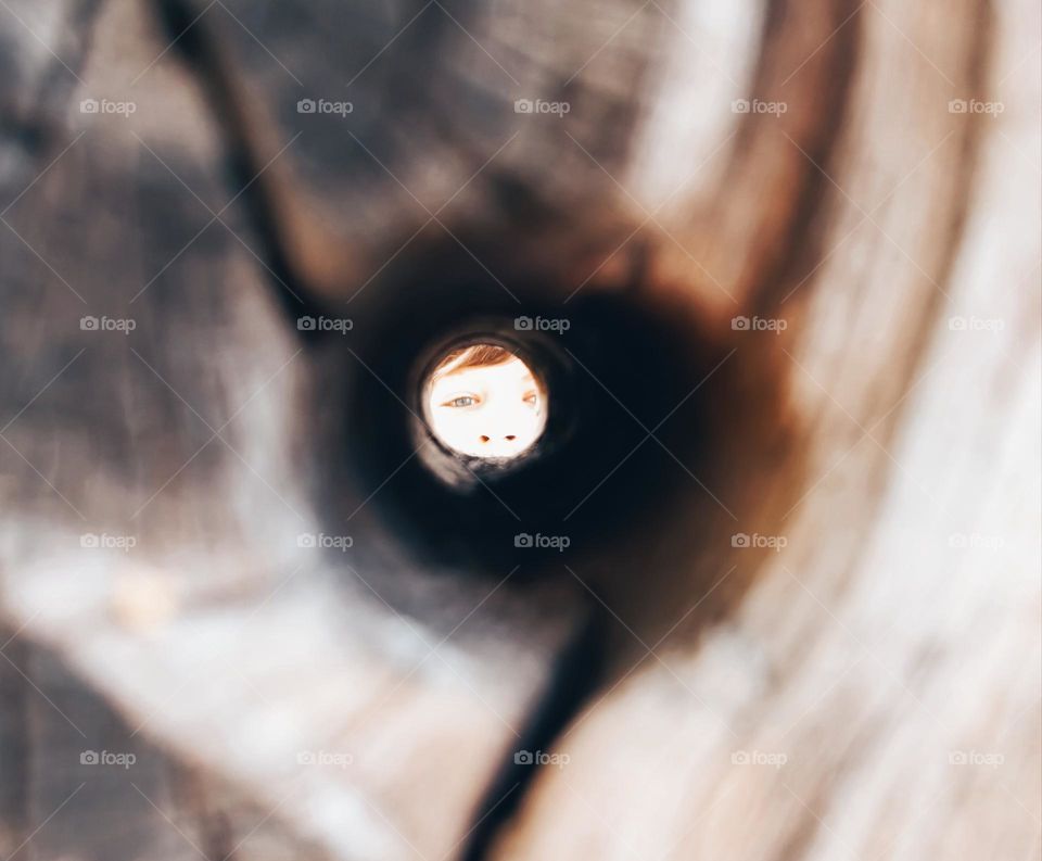 Close up of a wooden hole with a face at the end of the tunnel