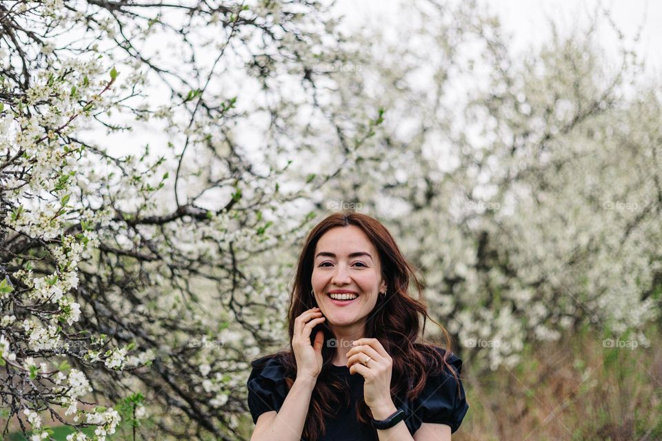 Joyfully smiling woman being surrounded by blossom trees, while on a walk, during springtime.
