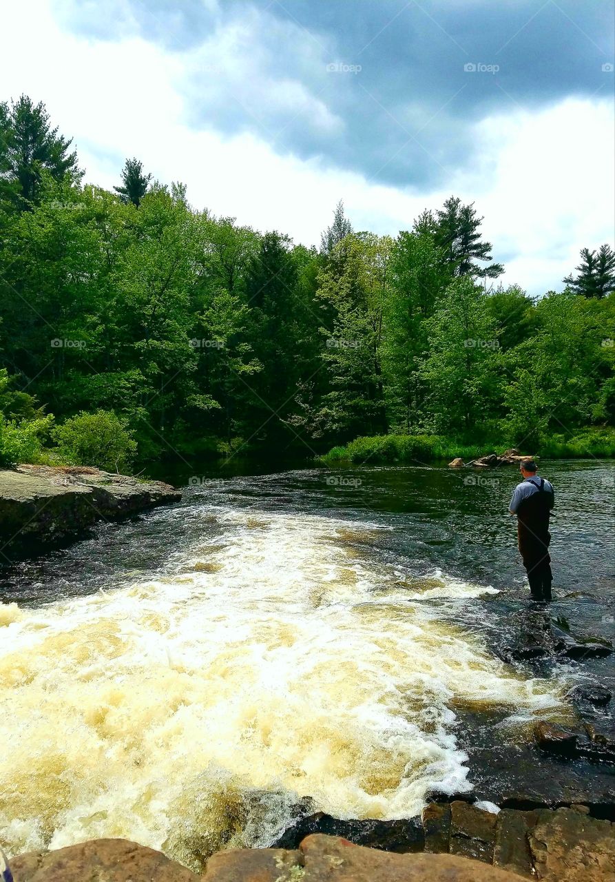 man fishing in fast flowing river off hiking trail