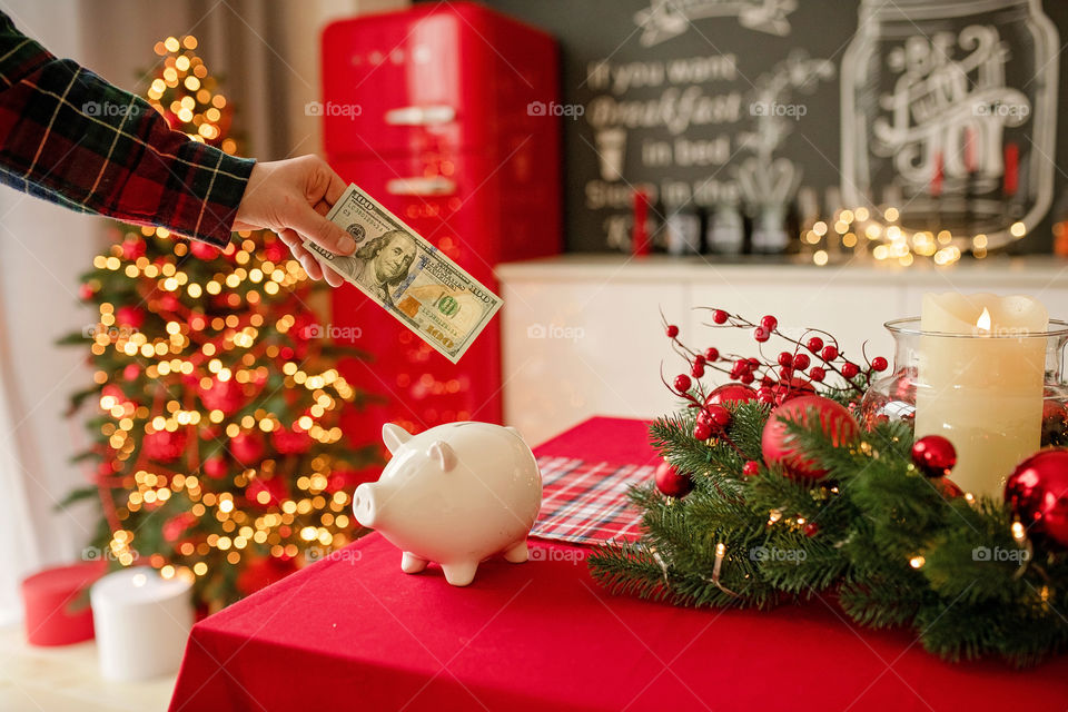 piggy bank with 100 dollars banknote in festive New Year atmosphere of scenery.  Magical bokeh with Christmas tree and bright lights.