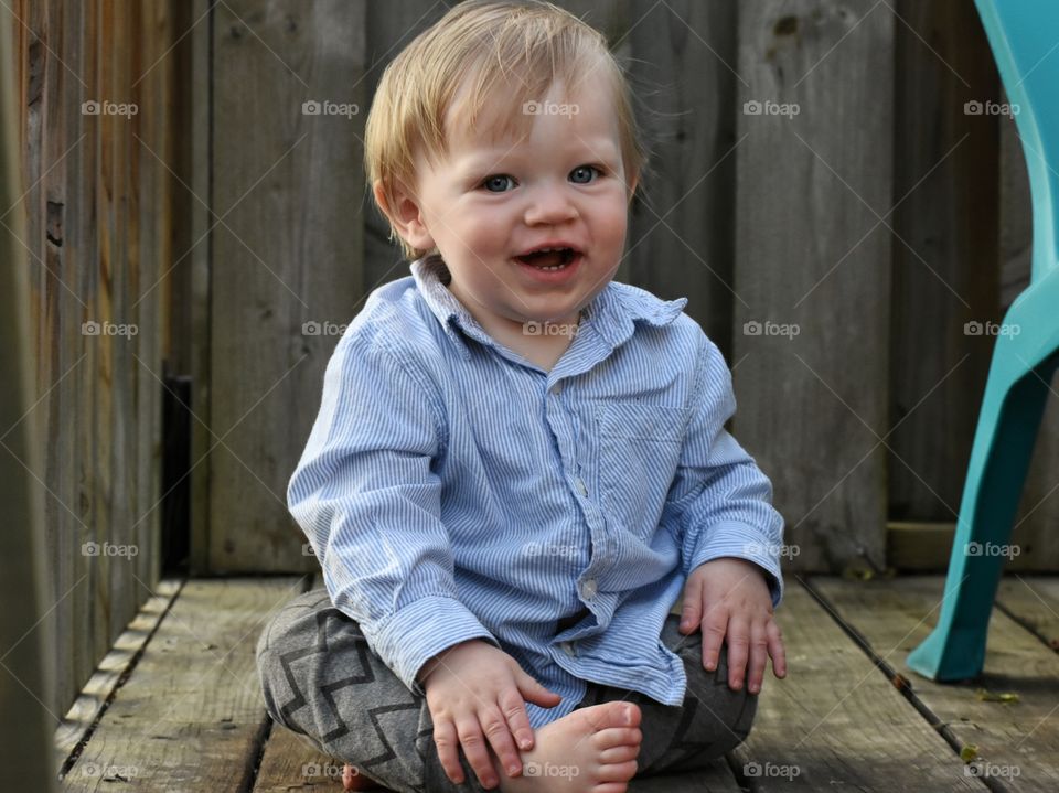 Cute happy barefoot toddler boy playing and laughing on wooden porch 