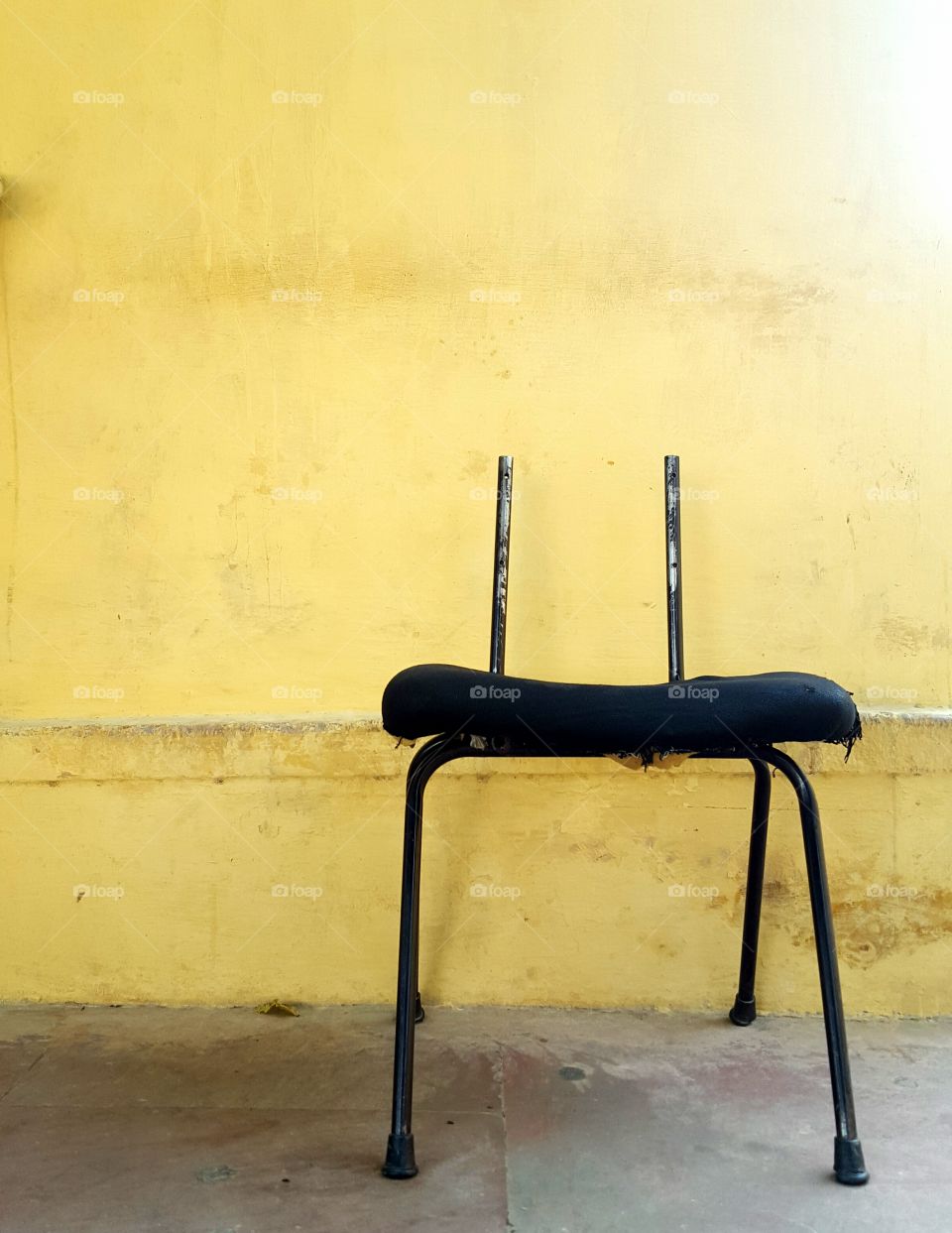 Broken Metal chair against a yellow Indian wall