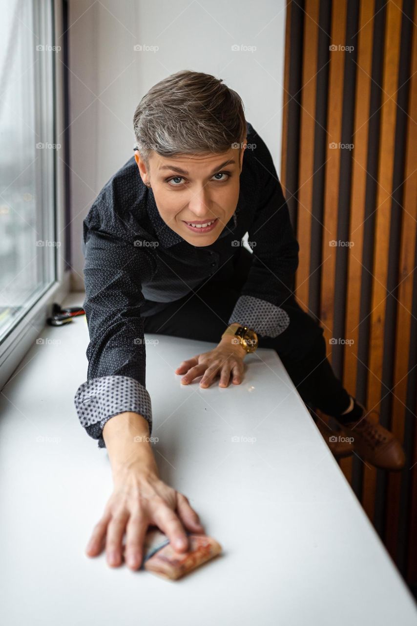A business woman with a short haircut is sitting on the windowsill, a beautiful portrait looking into the camera, beautiful eyes