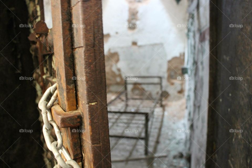 Looking through chained door at old bed in abandoned jail cell