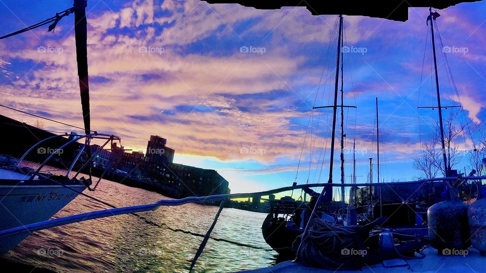 A spectacular night shot of sailboats w masts & other boats on the East River at Newtown Creek, LIC, Queens w clouds at twilight time reflecting from the waters below & back above in delightful shades of violet & purple. 2021. Hypnotic Productions