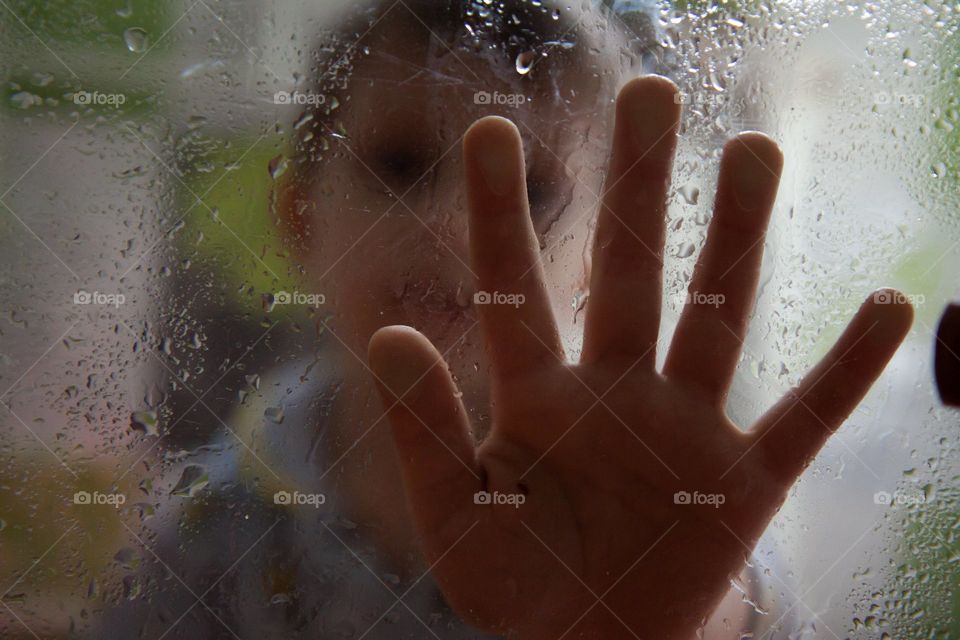sad portrait of a boy through wet glass