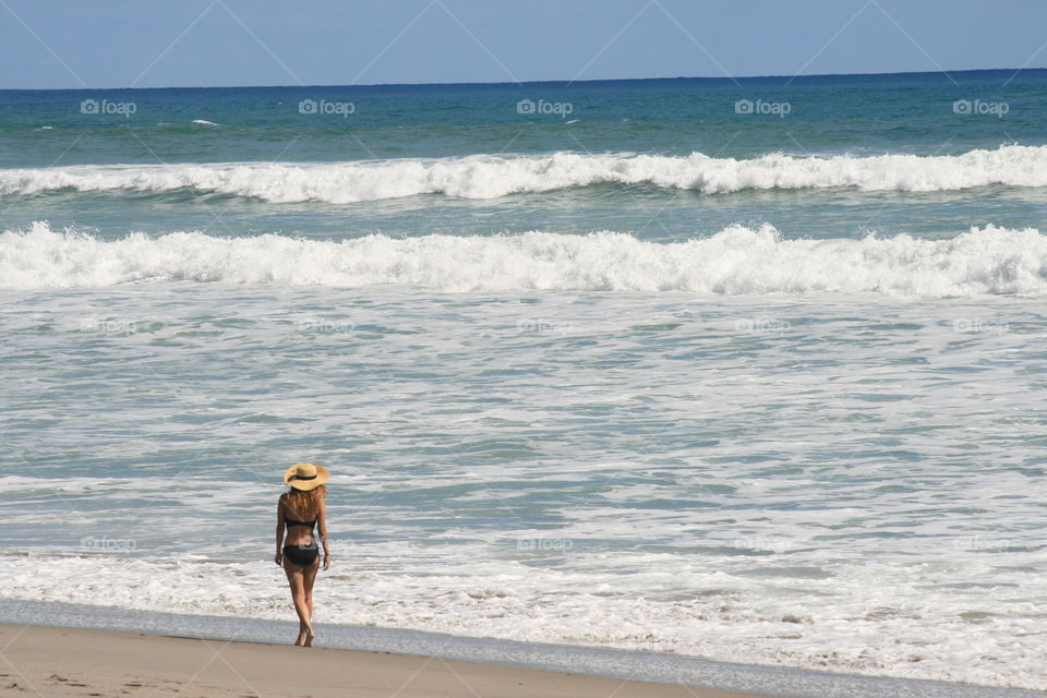 Female walking along a sandy beach looking out over the clear blue ocean. Vacation getaway to a Tropical Seaside Paradise.