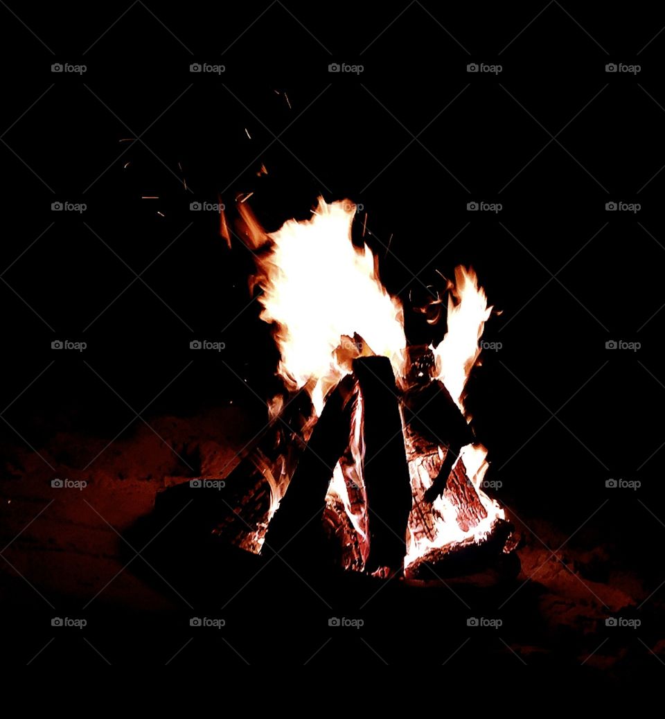 a bright flaming bonfire in a firepit on the sandy beach