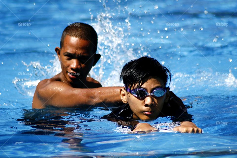 young kid learns how to swim with the help of a swimming coach