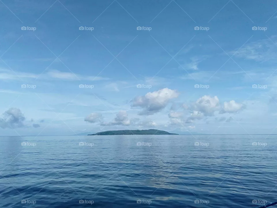 Island in the stream underneath the baby blue skies and clouds with relaxing calm sea.