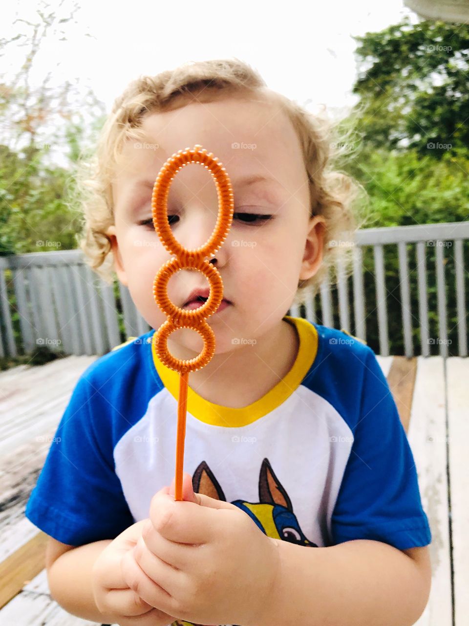 Toddler boy blowing bubbles outside on the deck having fun