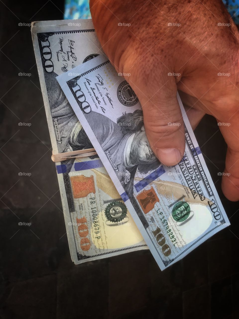 A hand holding several crisp new one hundred dollar bills