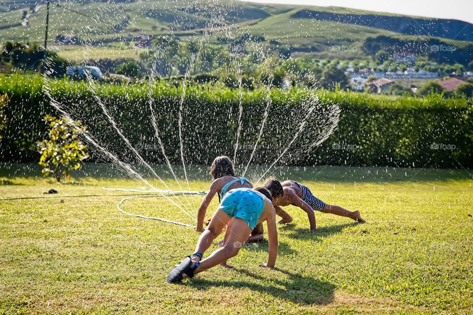 Children play with a water sprinkler in the garden