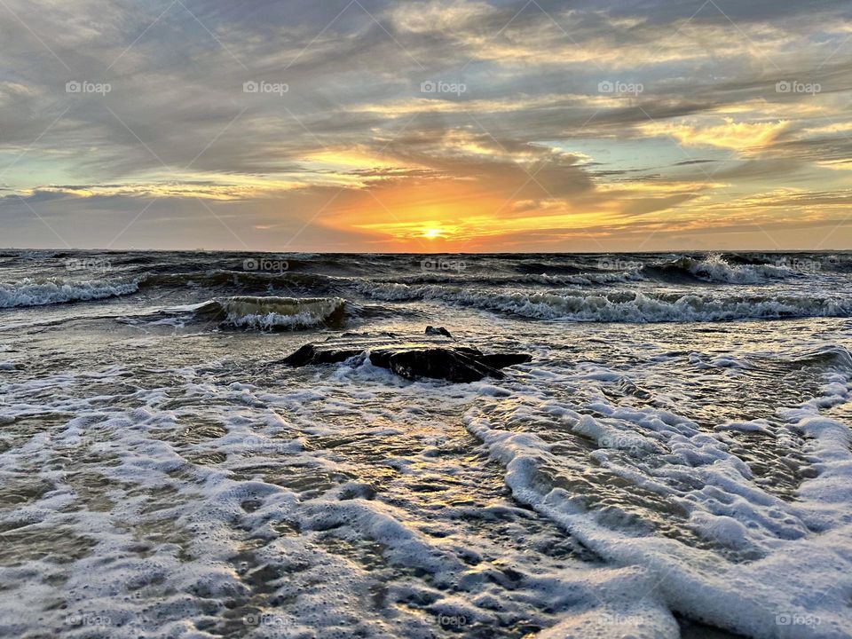 A breathtaking and radiant sunset which colors the waves iridescent, often towers and collides the shore with great force. The impact of the waves and foam against the coastline created a stunning display of energy and motion