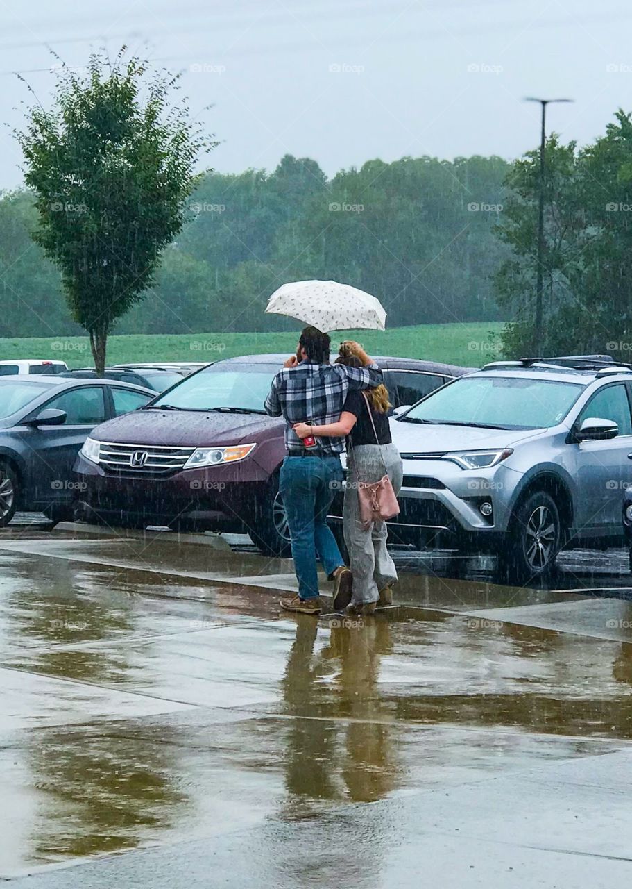 Couple in love walking in the rain with an umbrella to a parking lot of cars
