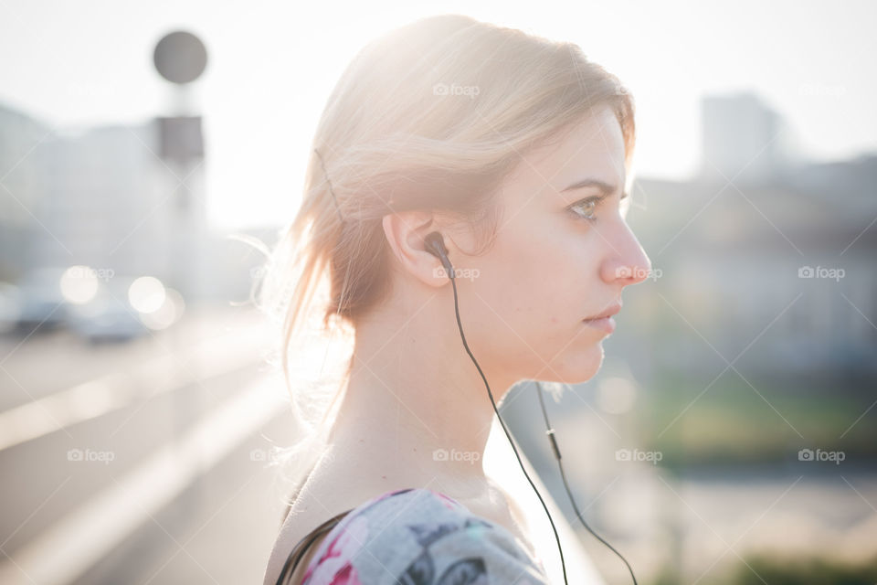 young and beautiful blonde woman in the street listening to music with earphones