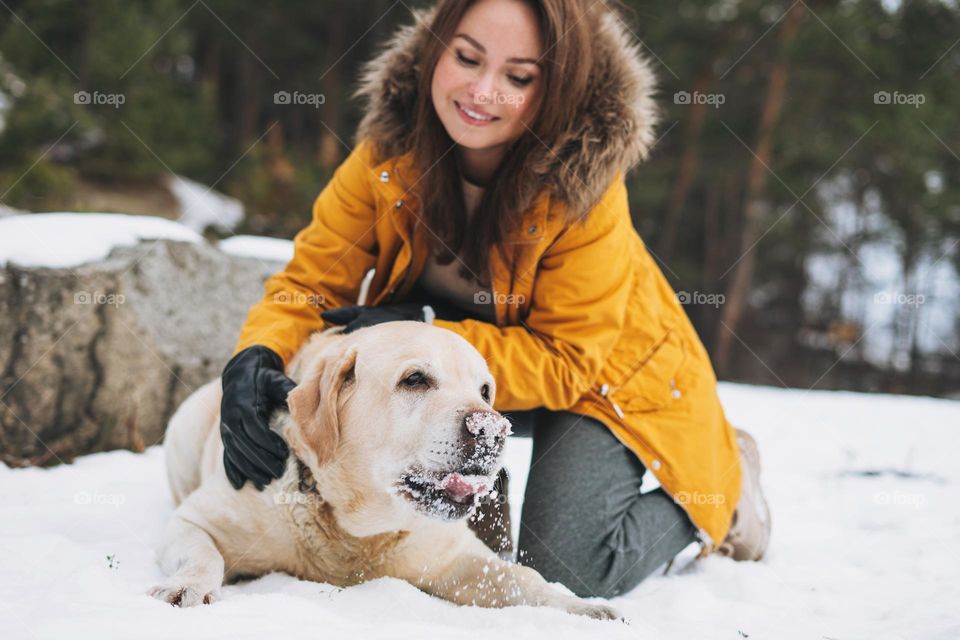 Young smiling woman in yellow jacket with big kind white dog Labrador walking in the winter forest