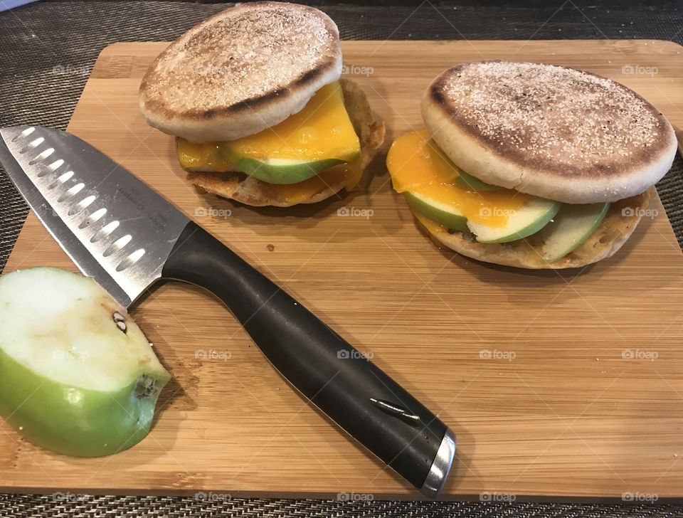 A delicious English muffin with apples and cheese melted inside displayed on a cutting board with a knife and apple slices in the kitchen. USA, America