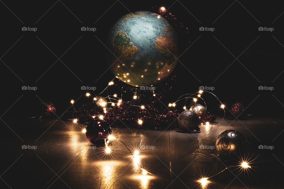 a festive portrait of a globe on a wooden floor surrounded by fairy lights and other christmas ornaments. ready for a global most wonderful time of the year. created by light painting all the different elements.