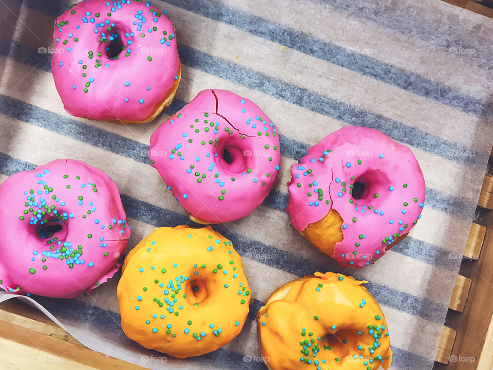 Six yellow and pink donuts with colorful sprinkles 