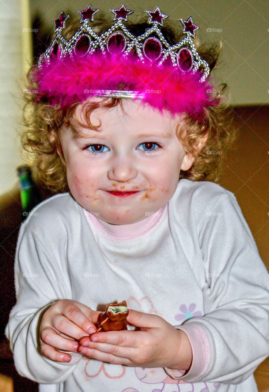 Little girl in princess tiara is most happy when eating chocolate 