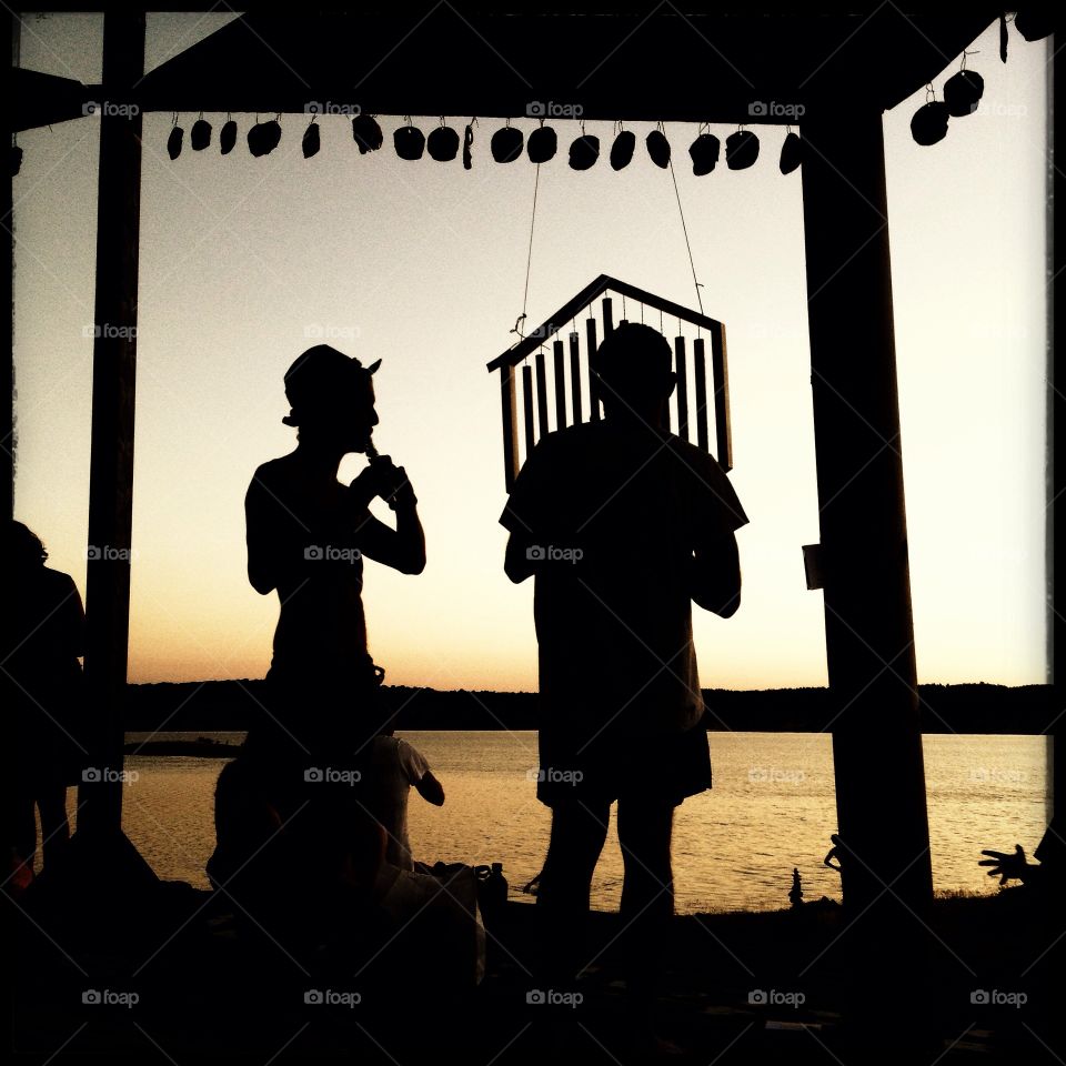 Silhouette of two musicians playing in front of a lake