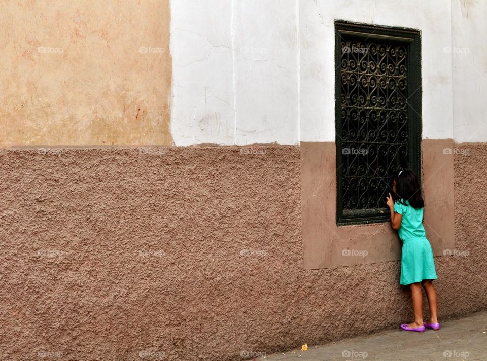 Little girl dressed in green looks through the bars of a window in one of the narrow streets of Marrakesh in Morocco