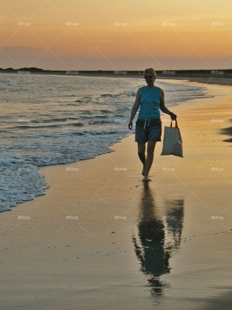 Beachcomber at sunset . A lone beachcomber walks the beach at sunset