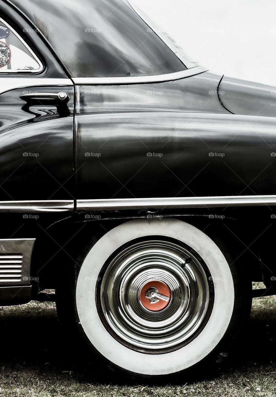 The rear, side of a black vintage car with a red logo on its tires
