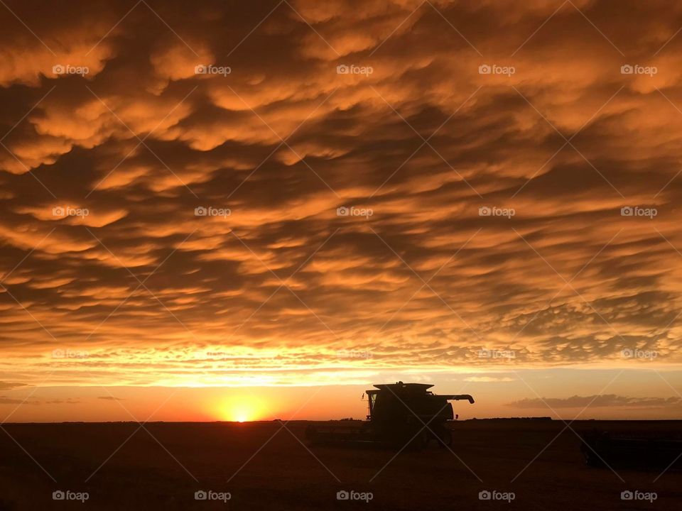 Orange sunset sinking down behind John Deere 