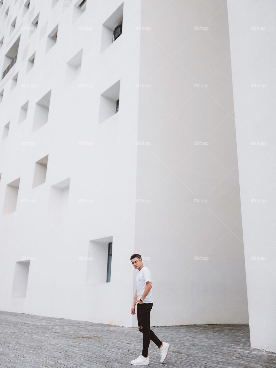 A man with white tee is walking in front of an artistic, geometric, white architecture