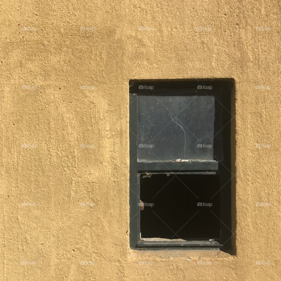 Golden yellow rustic wall with half open window into horse stable.