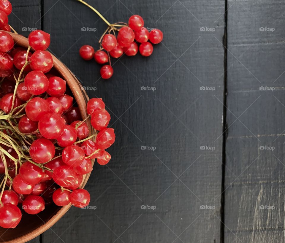 branch of red viburnum in an earthenware dish on a wooden black surface, top view