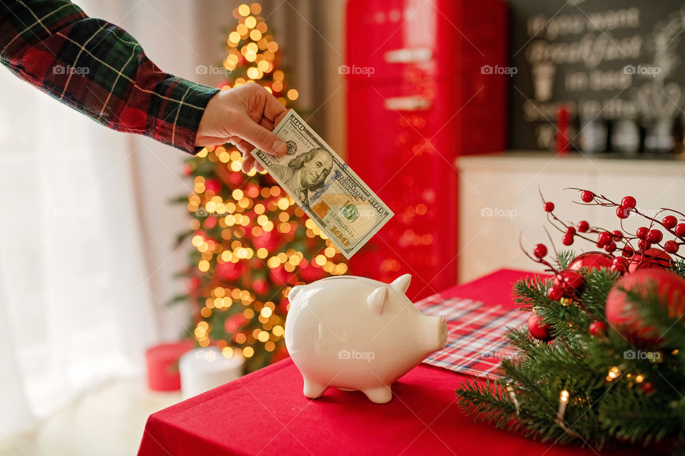 piggy bank with 100 dollars banknote in festive New Year atmosphere of scenery. Magical bokeh with Christmas tree and bright lights.