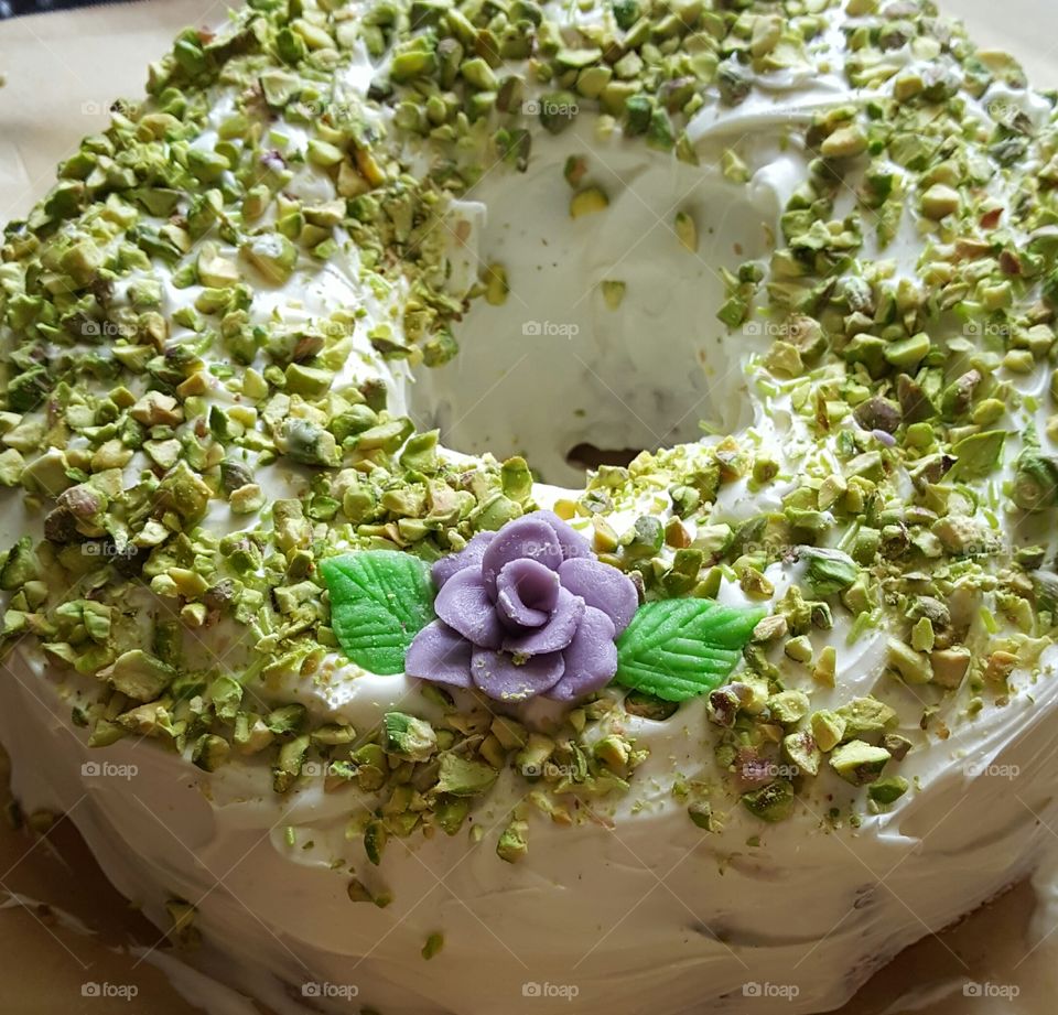 Pistachio cake with almond frosting, crushed pistachio nuts, and hand made chocolate rose and leaves