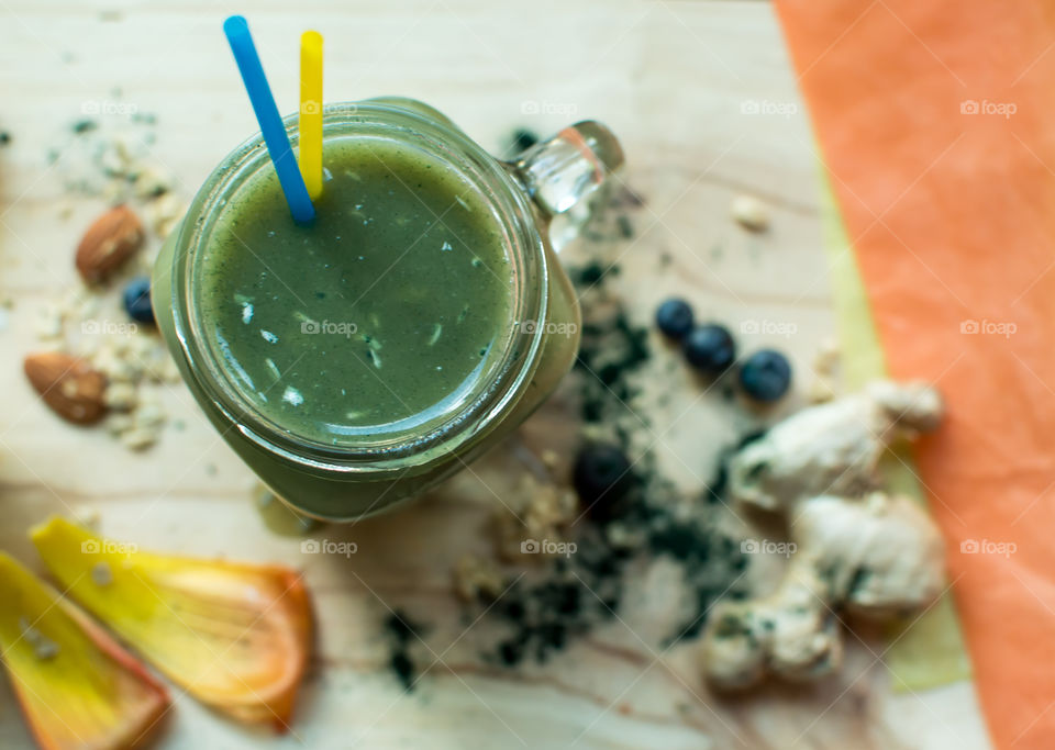 High angle view of green fruit smoothie wit spiroulina (spirulina) protein powder, coconut flakes, ginger root, blueberry, kiwi and almond butter 