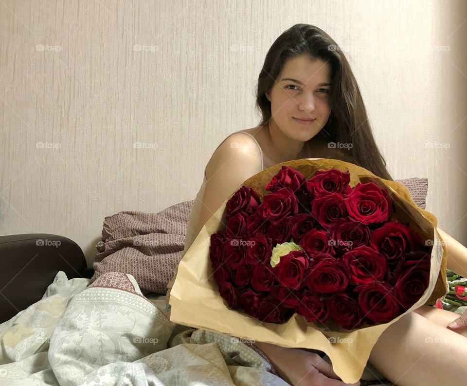 pretty girl sitting in bed with a huge bouquet of roses