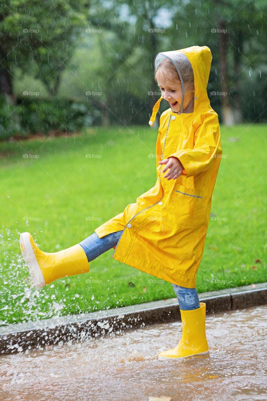 Happy kid in yellow raincoat having fun in puddle 