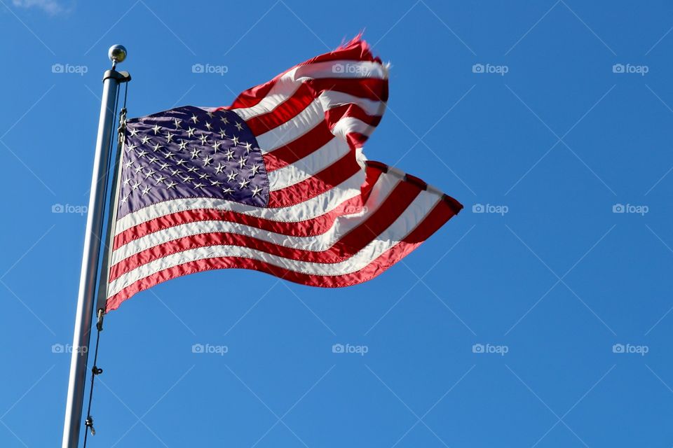 American flag high on flagpole blowing in the breeze against a colourful vivid blue clear sky