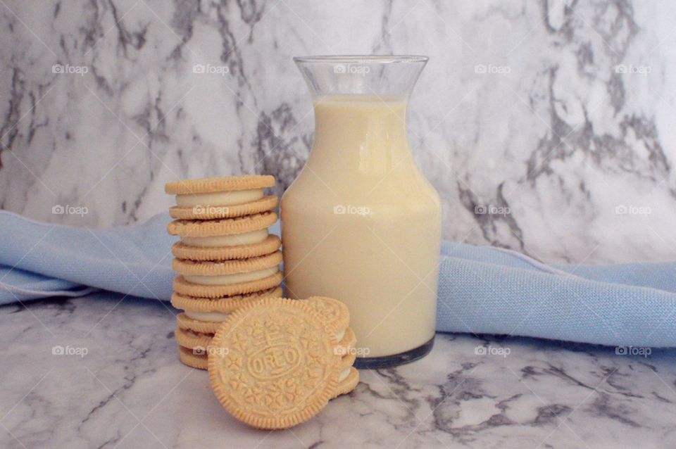 Oreo double stuff cookies stack next to a carafe of milk with a red and white straw on a marble backdrop