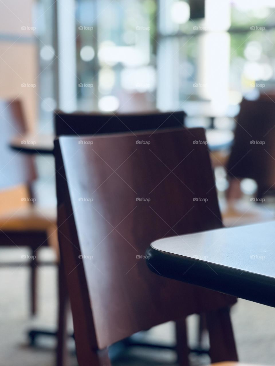 Cafe interior - clean lines closeup of hardbacked wooden chair and table edge with bokeh effect natural window light in background 