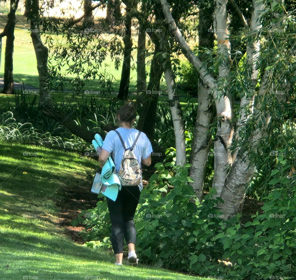 woman carrying a yoga mat walking to a favorite peaceful green area of an Oregon park near the duck pond