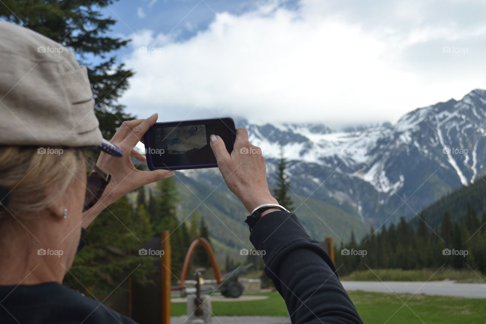 Woman with smartphone capturing photo of beautiful snowy Rocky Mountains 