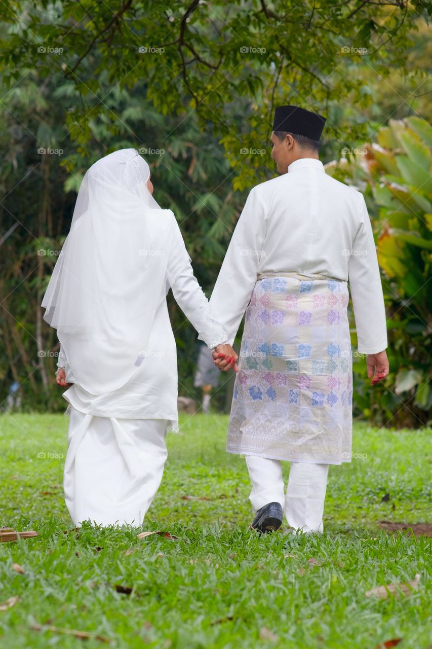 Bride and groom holding hands and walking together in the park.Love couple with love concept.Rear view.