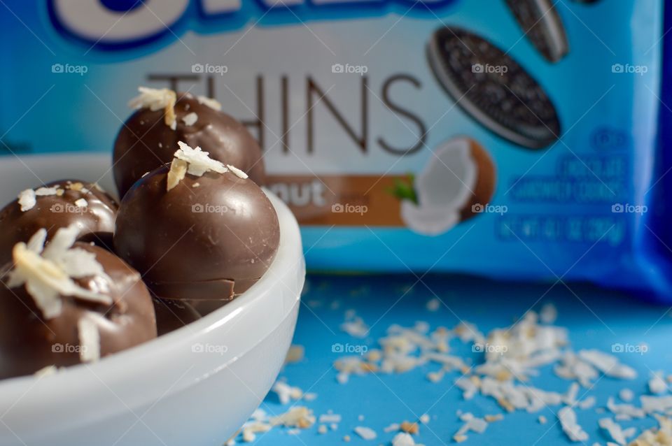 coconut Oreo thin cookies on a blue background with coconut shreds with truffles in a white bowl 