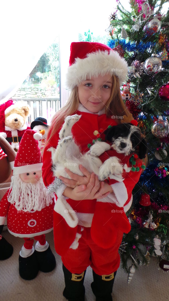 beautiful scene of a child dressed as santa claus holding a small puppy. looking