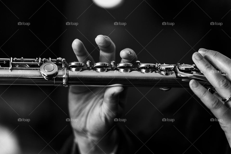 a black and white portrait of someone´s fingers releasing the valves of a silver flute. the flutist is playing a song.