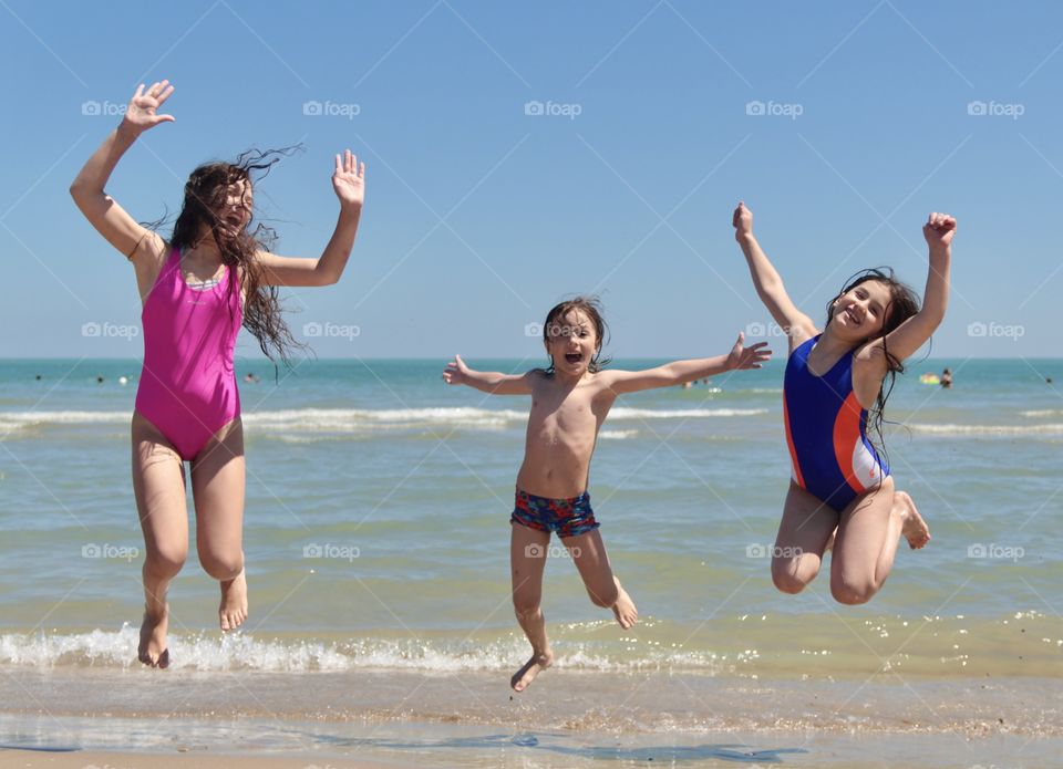 Three children jumping on the beach by the sea