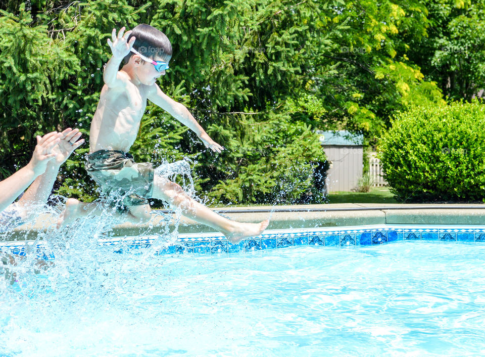 Young boy being thrown into a dug-out swimming pool with water splashing