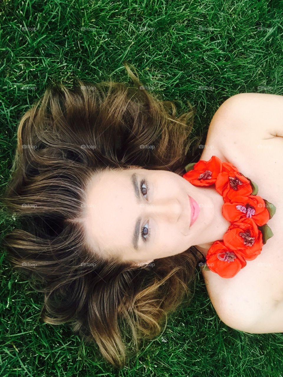 Portrait of dark blonde woman with poppies neckale laying on the grass 